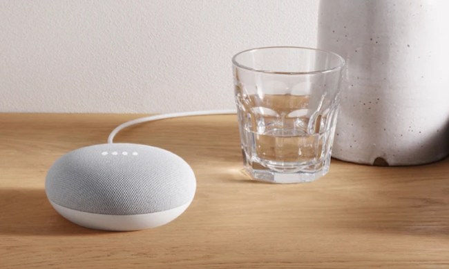 The Google Nest Mini on a table next to a glass of water.