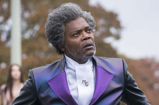 Samuel L. Jackson stares while wearing a purple suit.