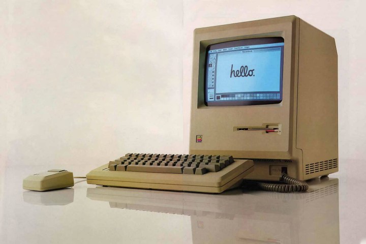 A classic Apple Macintosh shows a friendly hello on-screen.