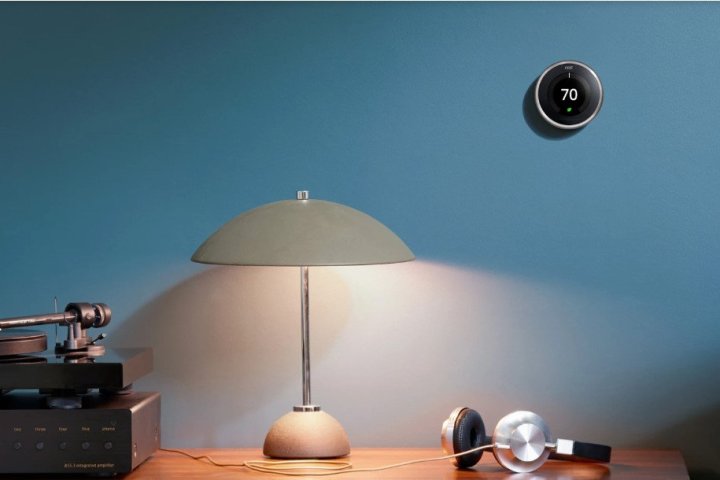 The Google Nest Learning Thermostat mounted on an office wall above a desk and lamp.