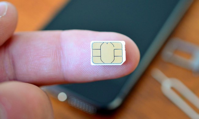 Sim chip on fingertip with phone in the background.