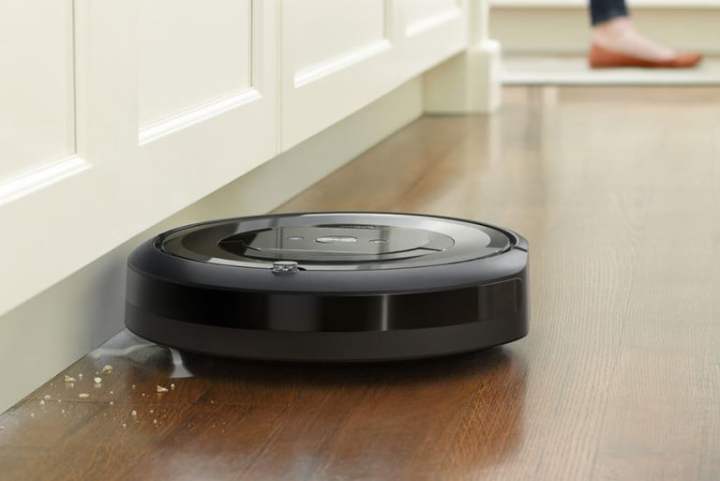 An iRobot Roomba e6 robot vacuum picks up crumbs from a hardwood floor.