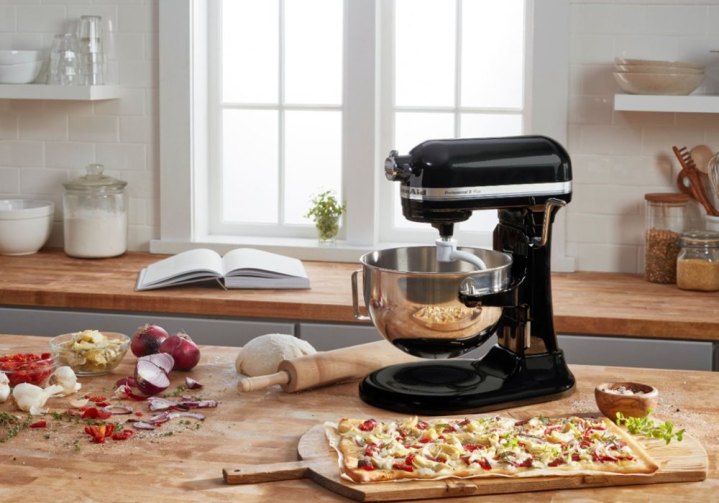 A blue KitchenAid Pro 5 Plus mixer sits on a kitchen counter mixing dough next to a flatbread pizza.