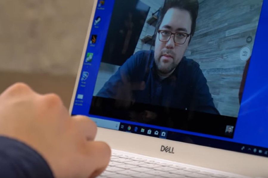 Close up of a person using a Dell laptop with their webcam turned on. The person's image is shown on the laptop screen.