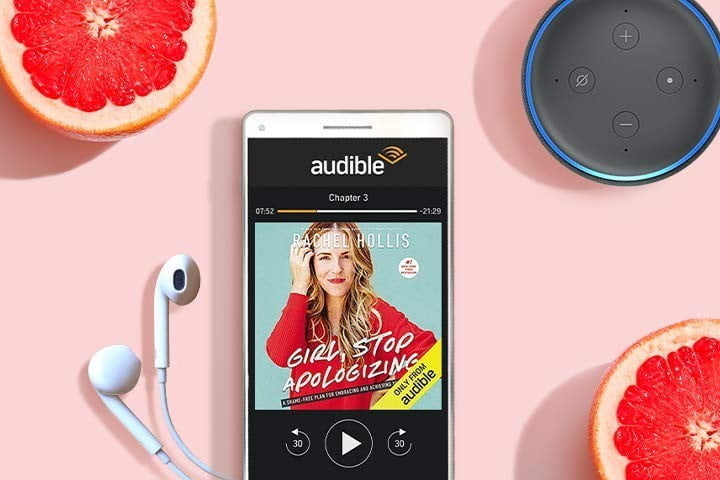 The Audible app on a smartphone showing an audiobook, with a pair of headphones and an Amazon Echo Dot alongside.