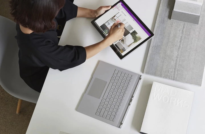 Vue de dessus d'une personne utilisant un ordinateur portable 2-en-1 comme une tablette, assise à un bureau blanc. 