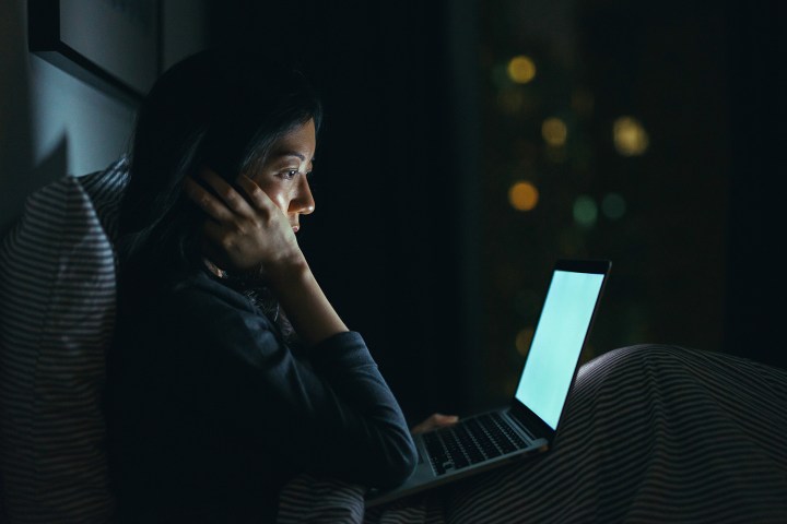 Mujer joven en pensamiento profundo mientras usa la computadora portátil en la cama por la noche.