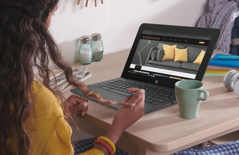 زنی با ژاکت زرد روی میز می نشیند که یک HP Chromebook 11.6 در مقابلش باز است و یک فنجان در کنار آن است.