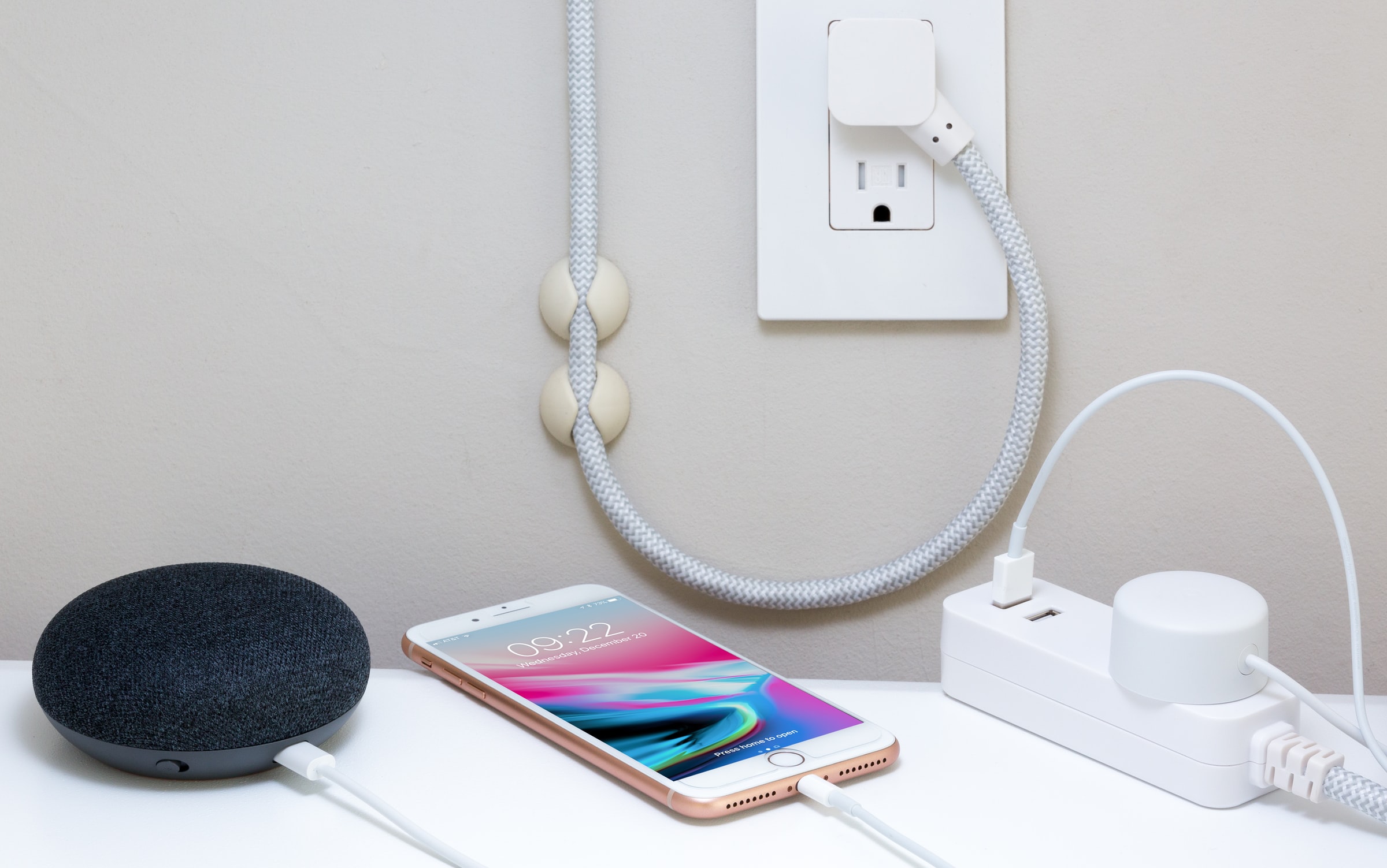 An iphone charging next to a smart home device and a power strip. 