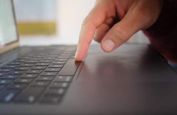 نمای جانبی مک بوک پرو اپل که انگشت روی صفحه کلید را نشان می دهد.