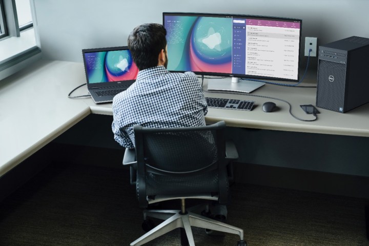A person works at a desk in front of a Dell UltraSharp 34 Curved Monitor hooked up to a laptop.