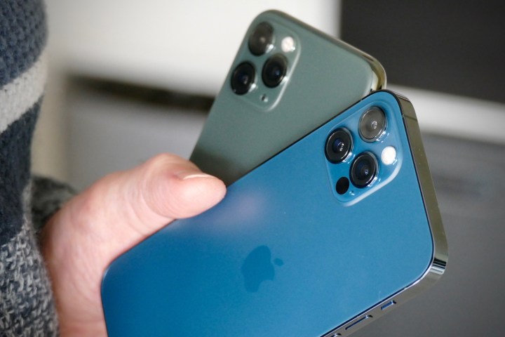 iPhone 11 Pro in Midnight Green with an iPhone 12 Pro in Pacific Blue in hand showing off camera modules.