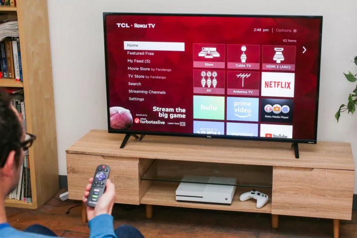 A person holding a remote towards the TCL 4 Series 4K TV.