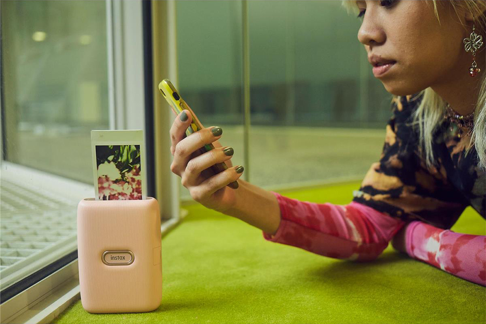 Mulher usando a impressora para smartphone Fujifilm Instax Mini Link com mulher segurando o iPhone.