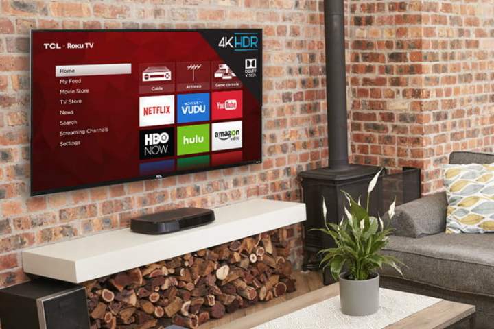 A wall mounted TCL 4 series 4k TV on a brick wall with living room items surrounding it.