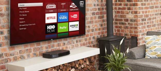 A TCL 4 Series 4k TV wall-mounted on a brick based wall with living room items surrounding it.