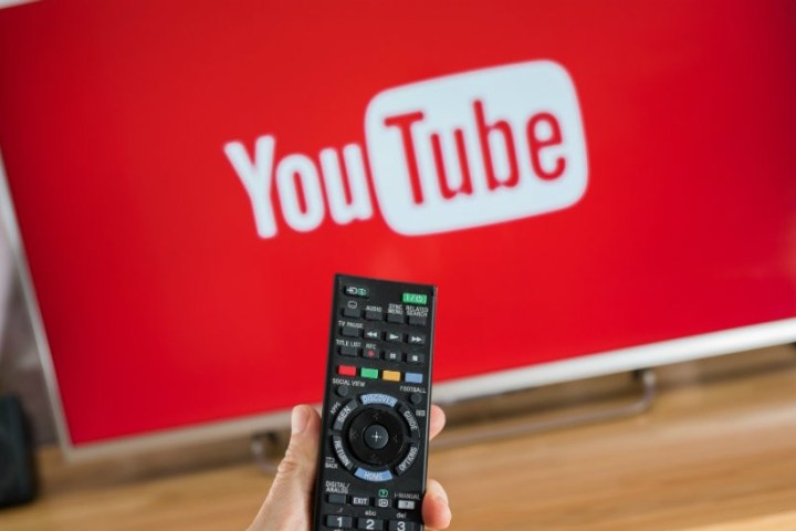 A person pointing a remote towards a TV with YouTube running.