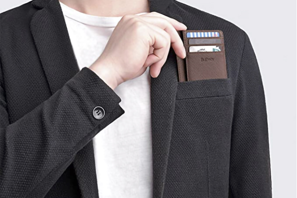 A man slides the Buffway Slim Minimalist smart wallet in brown into his jacket pocket. 