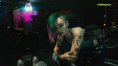 Judy leans over a table in Cyberpunk 2077.
