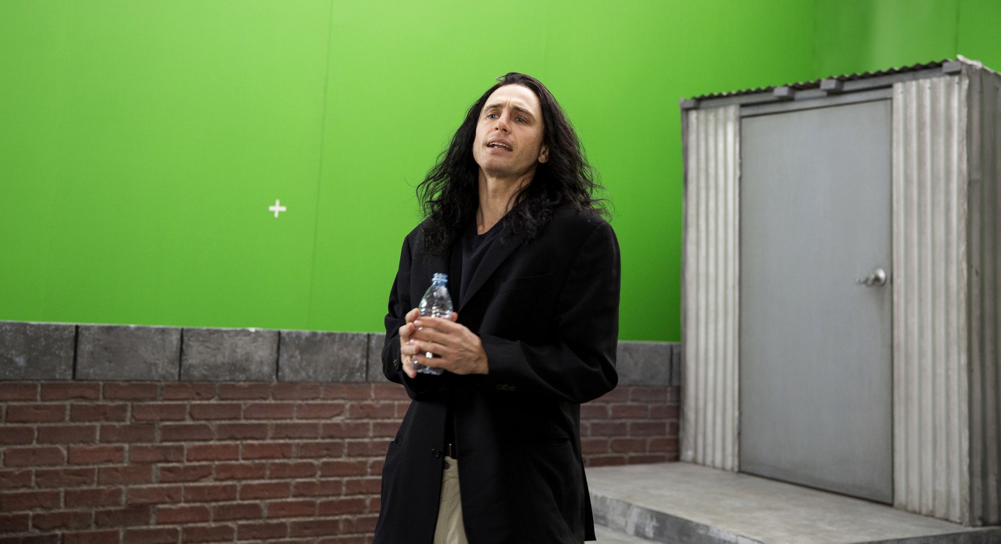 Un hombre sostiene una botella de agua y se para frente a una pantalla verde.