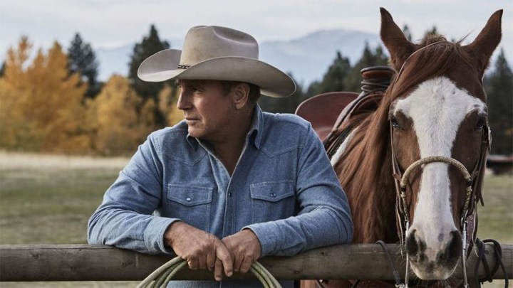 Kevin Costner en Yellowstone de pie junto a un caballo.