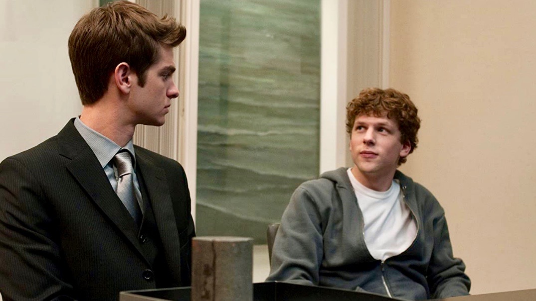 Andrew Garfield sits next to Jesse Eisenberg in The Social Network.