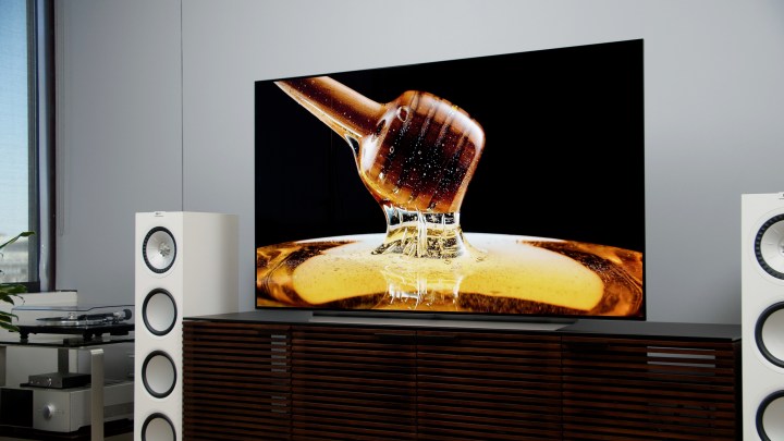 Th LG C1 OLED 4k TV with an image of honey on the screen, positioned in a home theater setting with speakers.