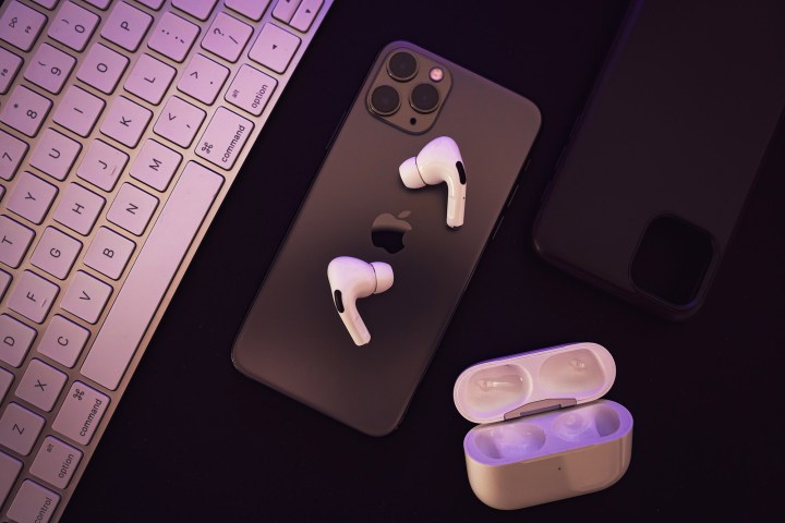 Airpods pro sitting on iphone with open charging case nearby. 