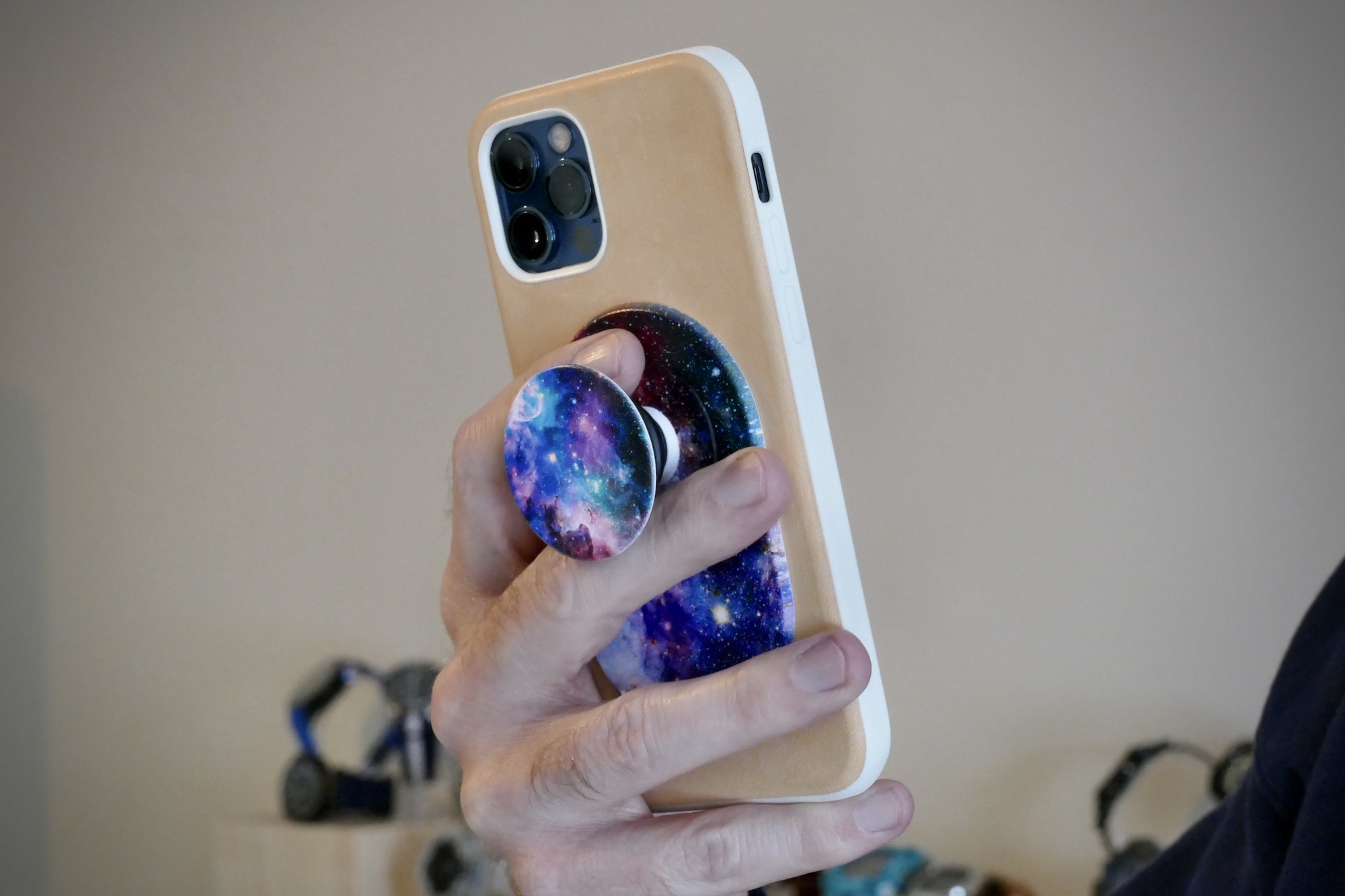 A hand holds an iPhone with a PopGrip attached.
