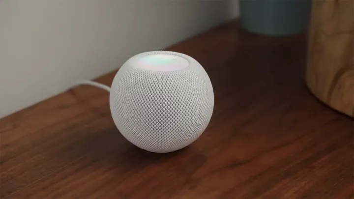 A white HomePod mini sitting on a desk.