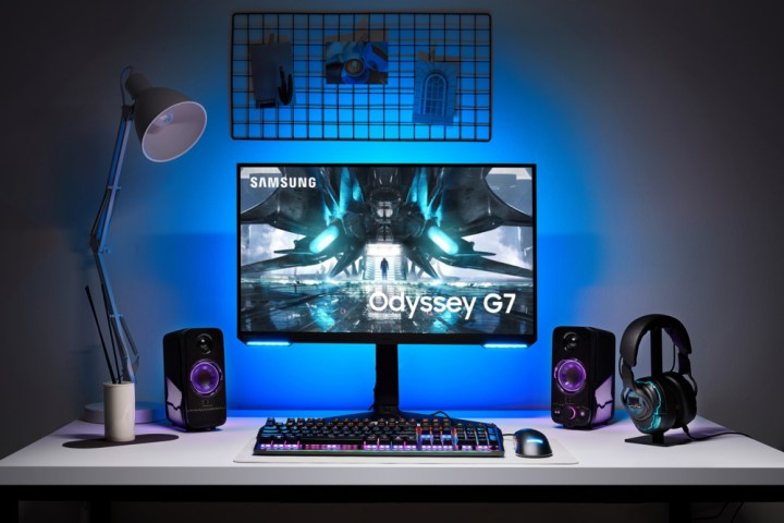 Samsung's new Odyssey G7 sits on a desk next to speakers, keyboard, mouse, and headphones.