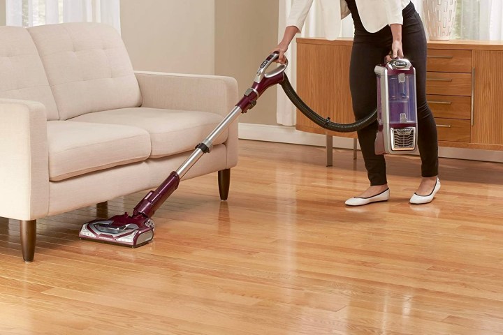 Woman using the Shark NV752 to vacuum under furniture.