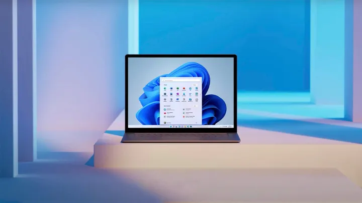 Una computadora portátil se encuentra en un escalón blanco, rodeada de iluminación blanca y azul. Ejecuta Windows 11.