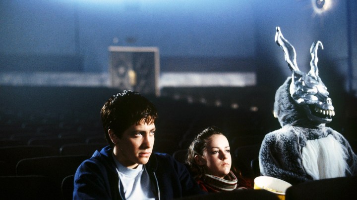 Donnie, Gretchen e Frank o coelho em um cinema vazio olhando para a tela em Donnie Darko.