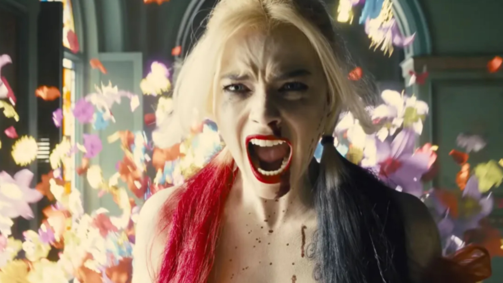 Margot Robbie como Harley Quinn, gritando cercada por flores no filme O Esquadrão Suicida.