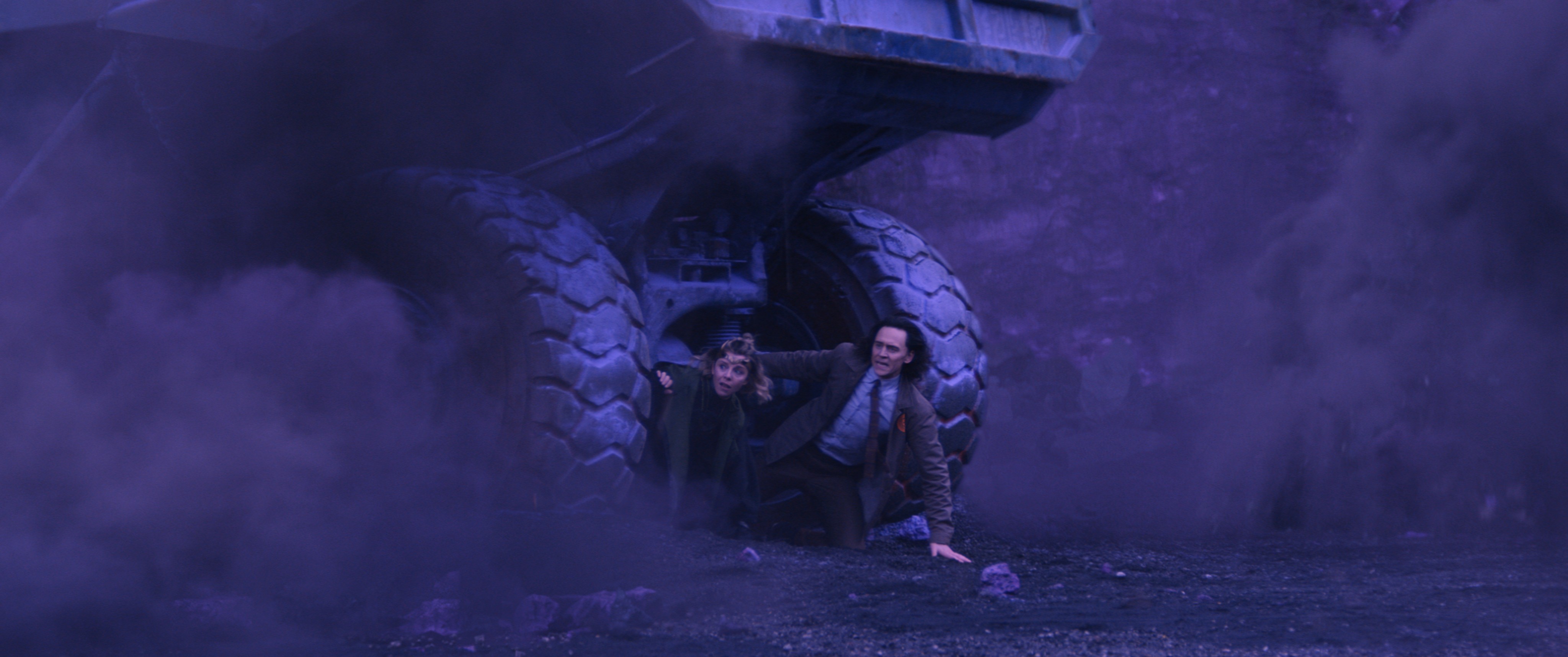 Sophia Di Martino e Tom Hiddleston se escondem sob um veículo de mineração na série Loki da Marvel.
