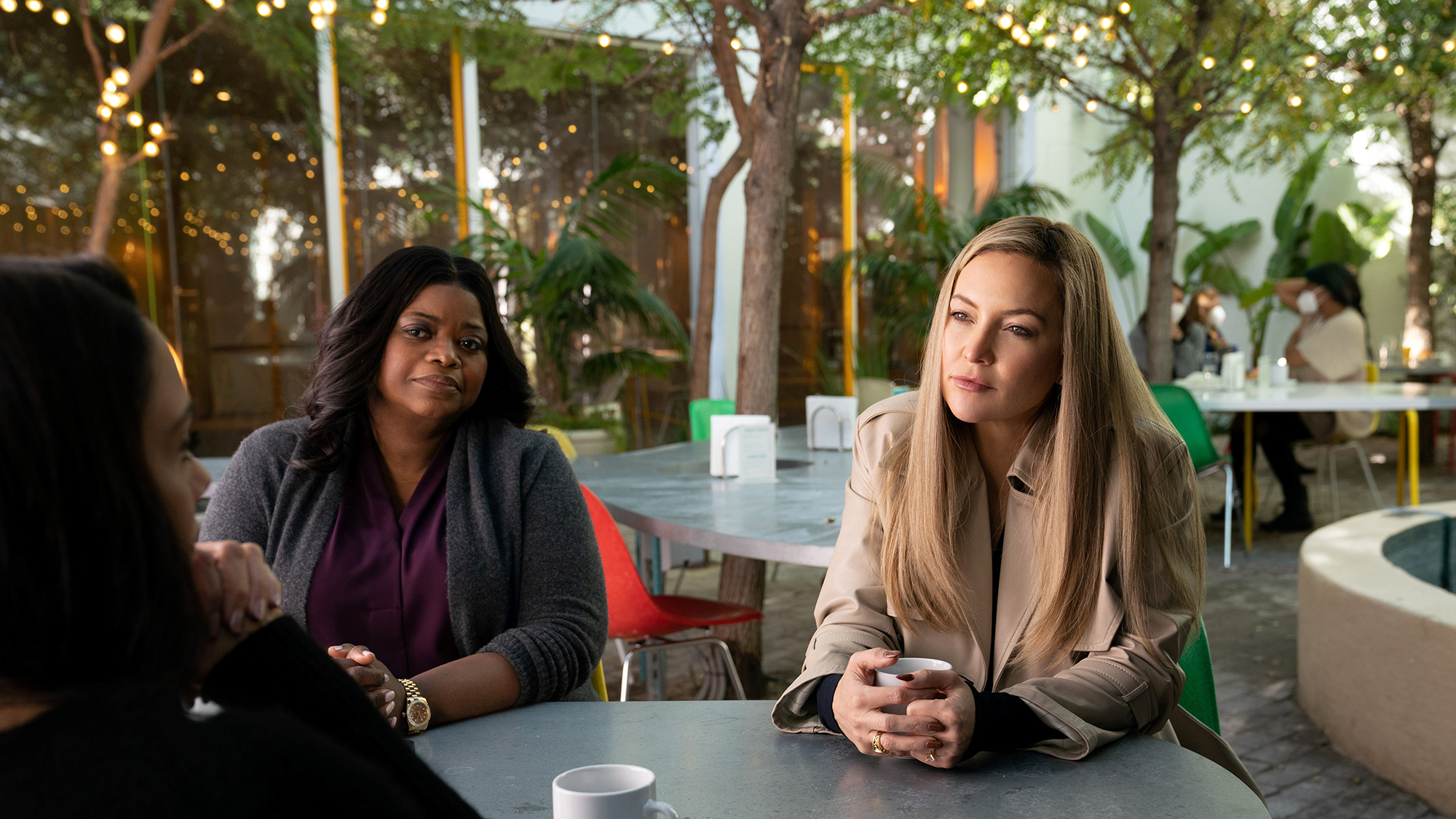 Kate Hudson e Octavia Spencer conversando com alguém em uma mesa em uma cena da segunda temporada de Truth Be Told.