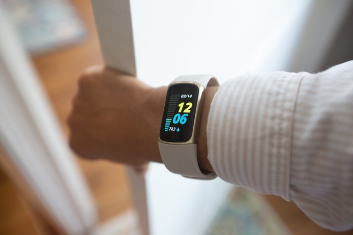 A Fitbit Charge 5 displaying the home screen on a wearer opening a door.