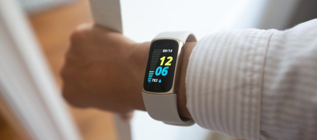 A Fitbit Charge 5 displaying the home screen on a wearer opening a door.