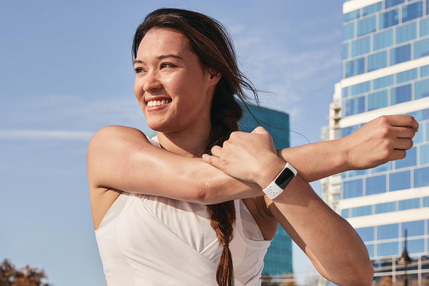 Uma mulher sorrindo ao ar livre usando roupas esportivas e um Fitbit Charge 5 no pulso.