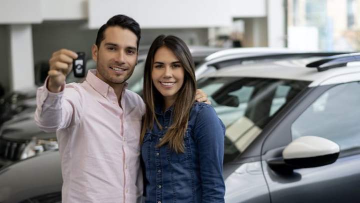 Happy couple buying a car at the dealership and holding the keys