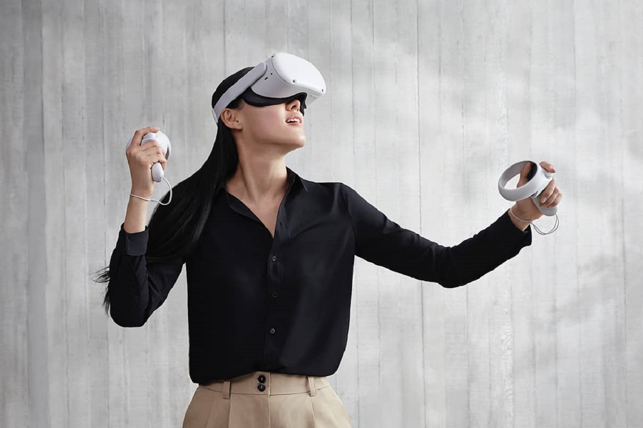 Uma pessoa usando um headset Oculus Quest 2 VR em frente a um fundo cinza.