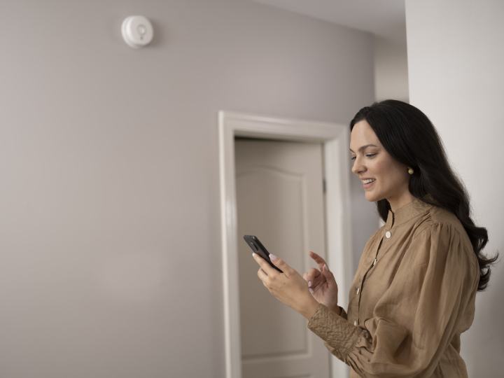 Woman connecting to Kidde Smoke + Carbon Monoxide Wi-Fi Alarm with smart features on phone.