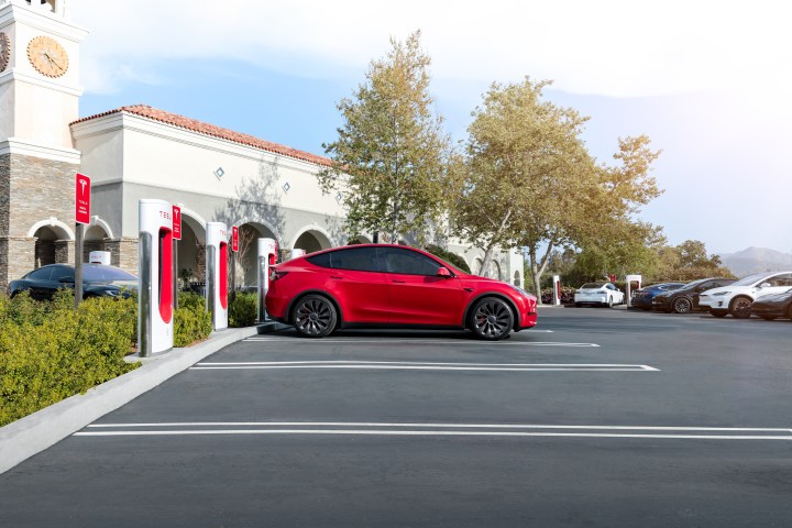 A red Tesla charging at a bank of Tesla Superchargers.