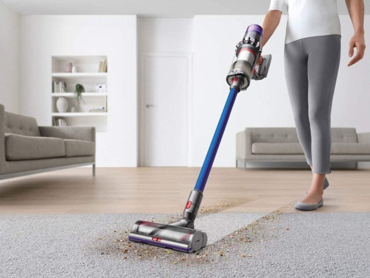 A person cleans a dirty living room carpet using a Dyson V11 Torque Drive Cordless Vacuum Cleaner.