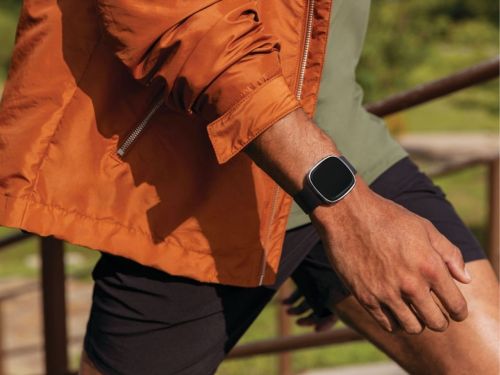The Fitbit Sense on a man's wrist while he walks outdoors.