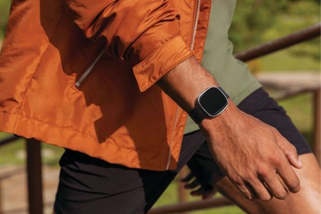 The Fitbit Sense on a man's wrist while he walks outdoors.