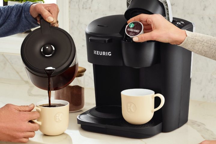 A Keurig K-Duo Essentials placed on a kitchen counter top while someone pours from it.