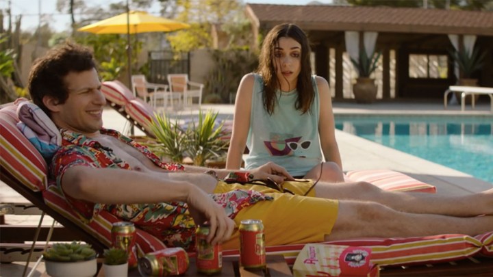 Andy Samberg lying on a chair by the pool with Cristin Milioti in a scene from Palm Springs.