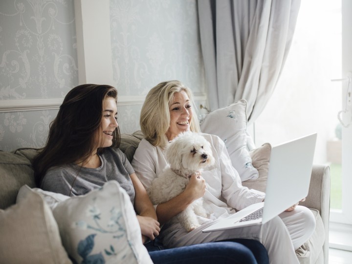 Two women video calling on their laptop with dog nearby protected by McAfee.